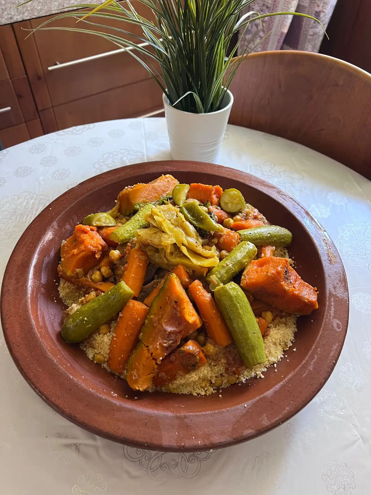 Traditional Moroccan couscous served in a clay dish with colorful vegetables and chickpeas on a white patterned tablecloth