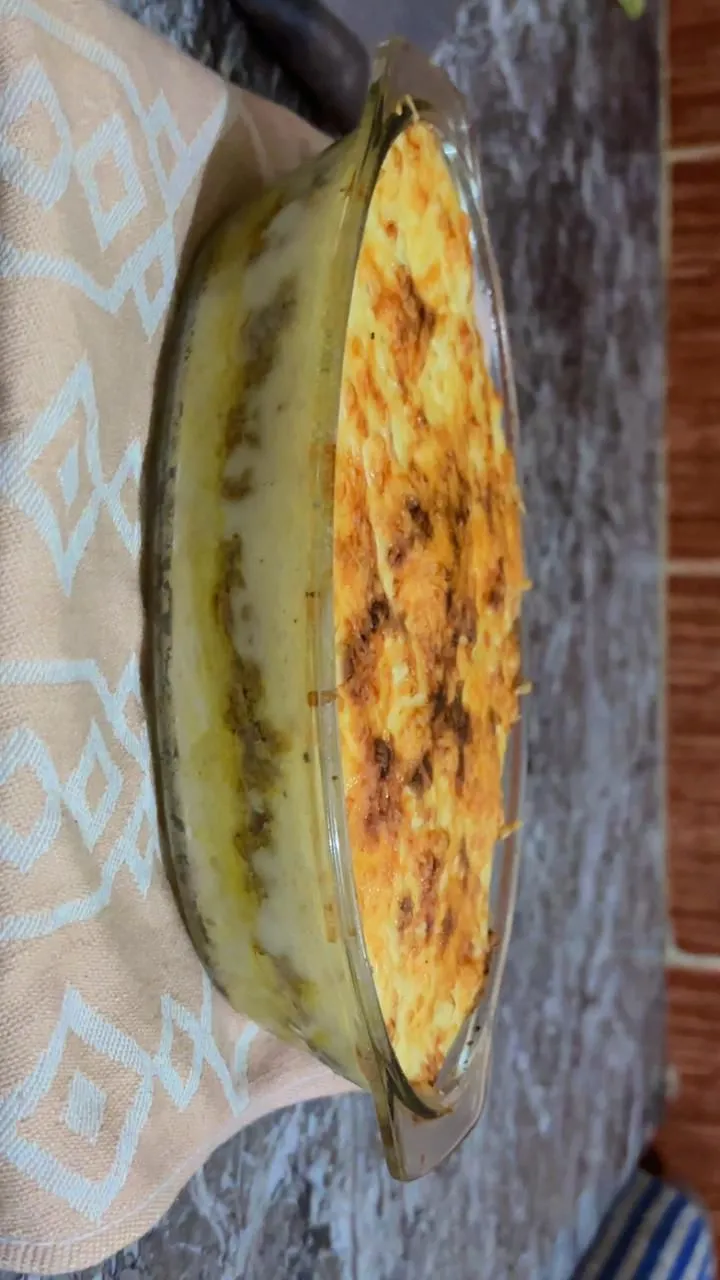 Seasoned ground beef sautéing with onions and herbs in a black pan with a wooden spoon on marble counter.