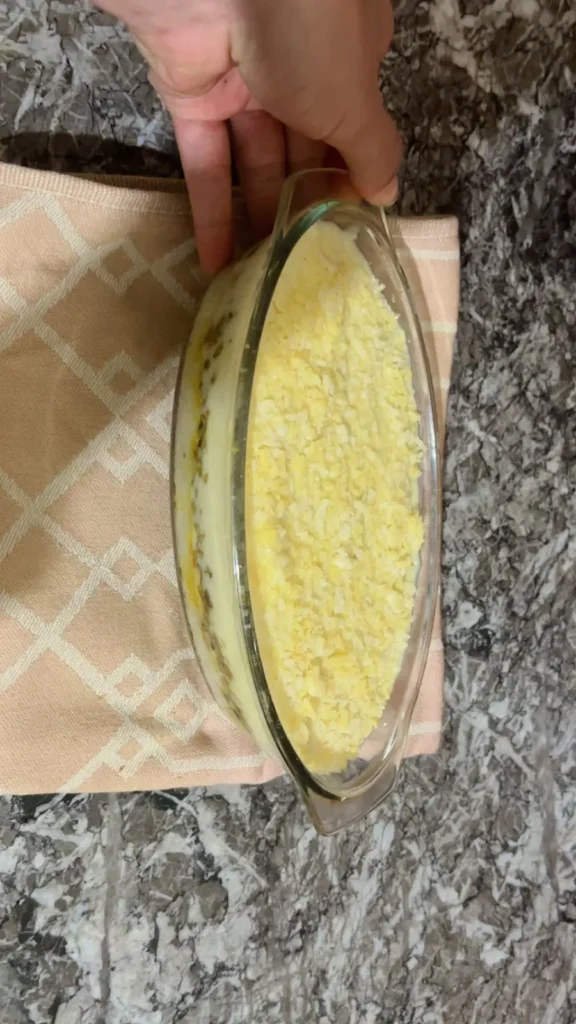 Casserole topped with grated cheese before baking, in oval dish on marble surface.
Title: Cheese Topping Before Baking, LunaChef