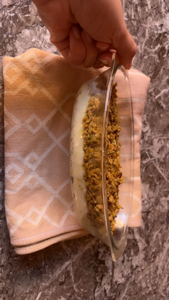 Hand holding oval dish showing a layer of seasoned ground beef over mashed potatoes.
Title: Layering Ground Beef Over Mashed Potatoes – LunaChef Recipe
