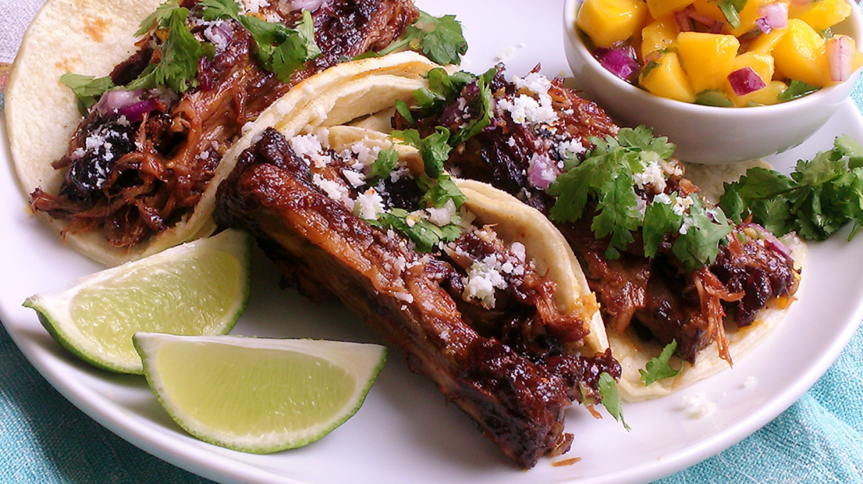 Pulled pork tacos topped with fresh mango salsa, cilantro, and lime, served in warm tortillas.